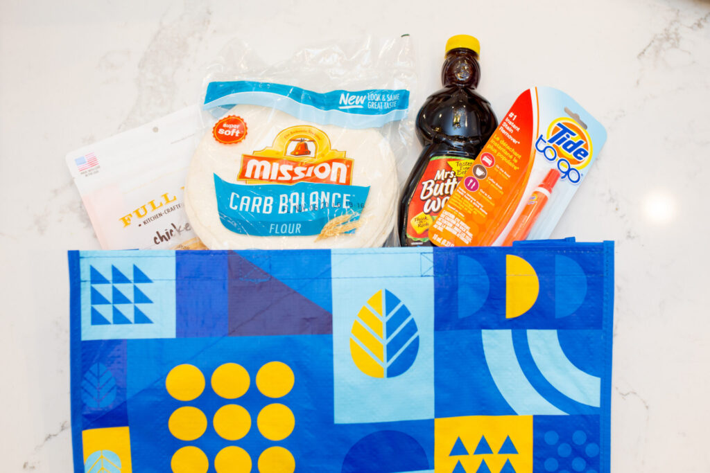 Walmart Membership by popular Nashville lifestyle blog, Hello Happiness: image of a reusable Walmart shopping bag filled with Mission Carb Balance tortillas, Mrs. Butterworth's syrup and Tide To-Go stick. 