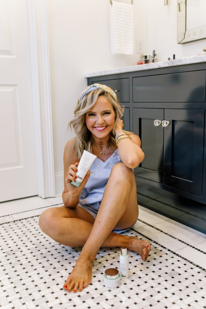 Clean Beauty Favorites: Dr Brandt Clean Biotic Review by popular Nashville beauty blog, Hello Happiness: image of woman sitting on her bathroom floor and holding some Dr. Brandt Clean Biotic beauty products.
