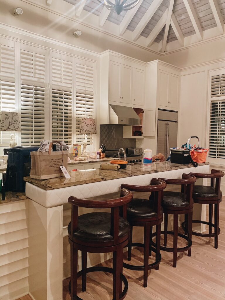 Rosemary Beach by popular Nashville travel blog, Hello Happiness: image of a kitchen with white plantation shutters, vaulted ceiling, and wooden barstools with black leather cushions. 