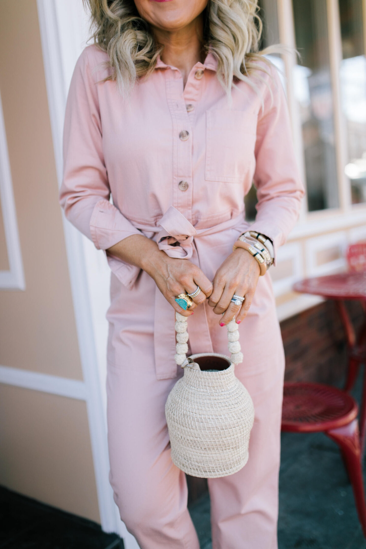 Splurge vs. Steal by popular Nashville fashion blog, Hello Happiness: image of Natasha Stoneking wearing a pink utility jumpsuit and holding a woven purse.