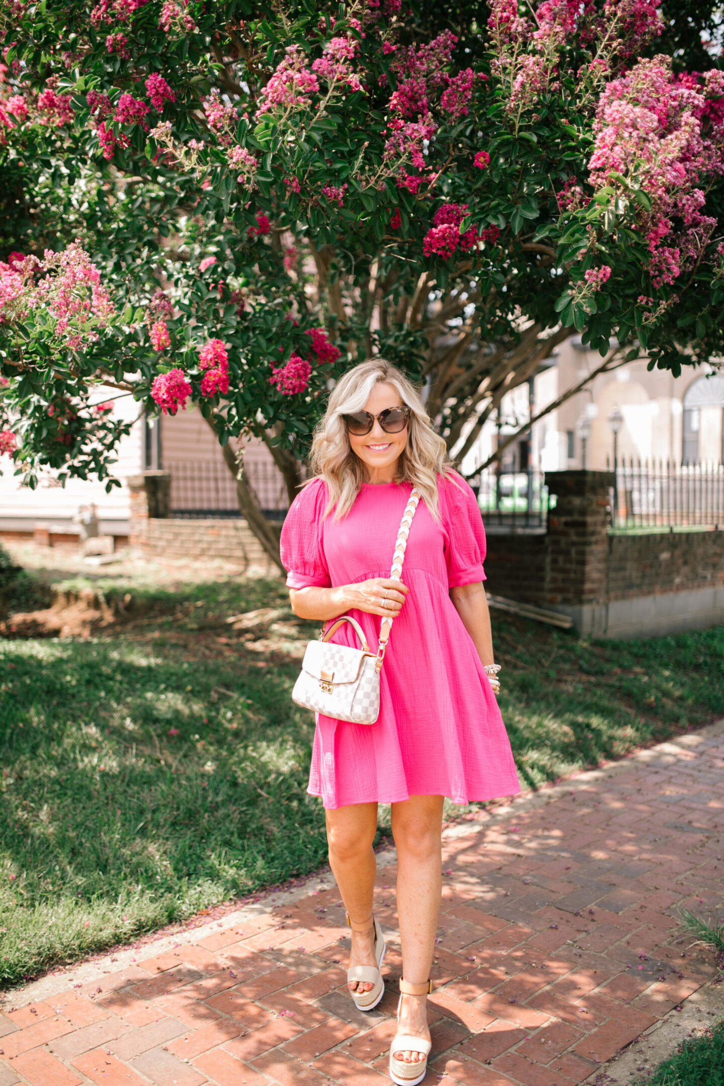 All About Me by popular Nashville lifestyle blog, Hello Happiness: image of Natasha Stoneking standing under a tree with pink blossoms and wearing a pink babydoll dress with tan strap espadrilles.