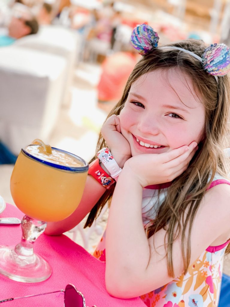 Happy 8th Birthday Daughter by popular Nashville lifestyle blog, Hello Happiness: image of a little girl wearing a sequin animal ears head band and sitting in front of a large orange drink. 