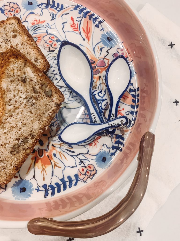 Good Eats | Cream Cheese Banana Bread Recipe by popular Nashville life and style blog, Hello Happiness: image of sliced cream cheese banana bread on a Anthropologie Eres serving dish, next to some Anthropologie Eres measuring spoons.