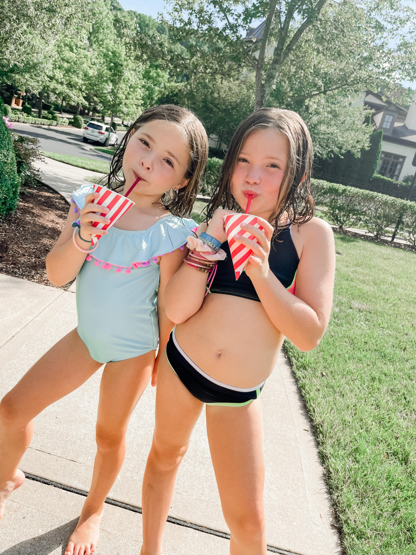 Walmart + Membership by popular Nashville lifestyle blog, Hello Happiness: image of two girls wearing swimsuits and eating snow cones in red and white stripe paper cups.