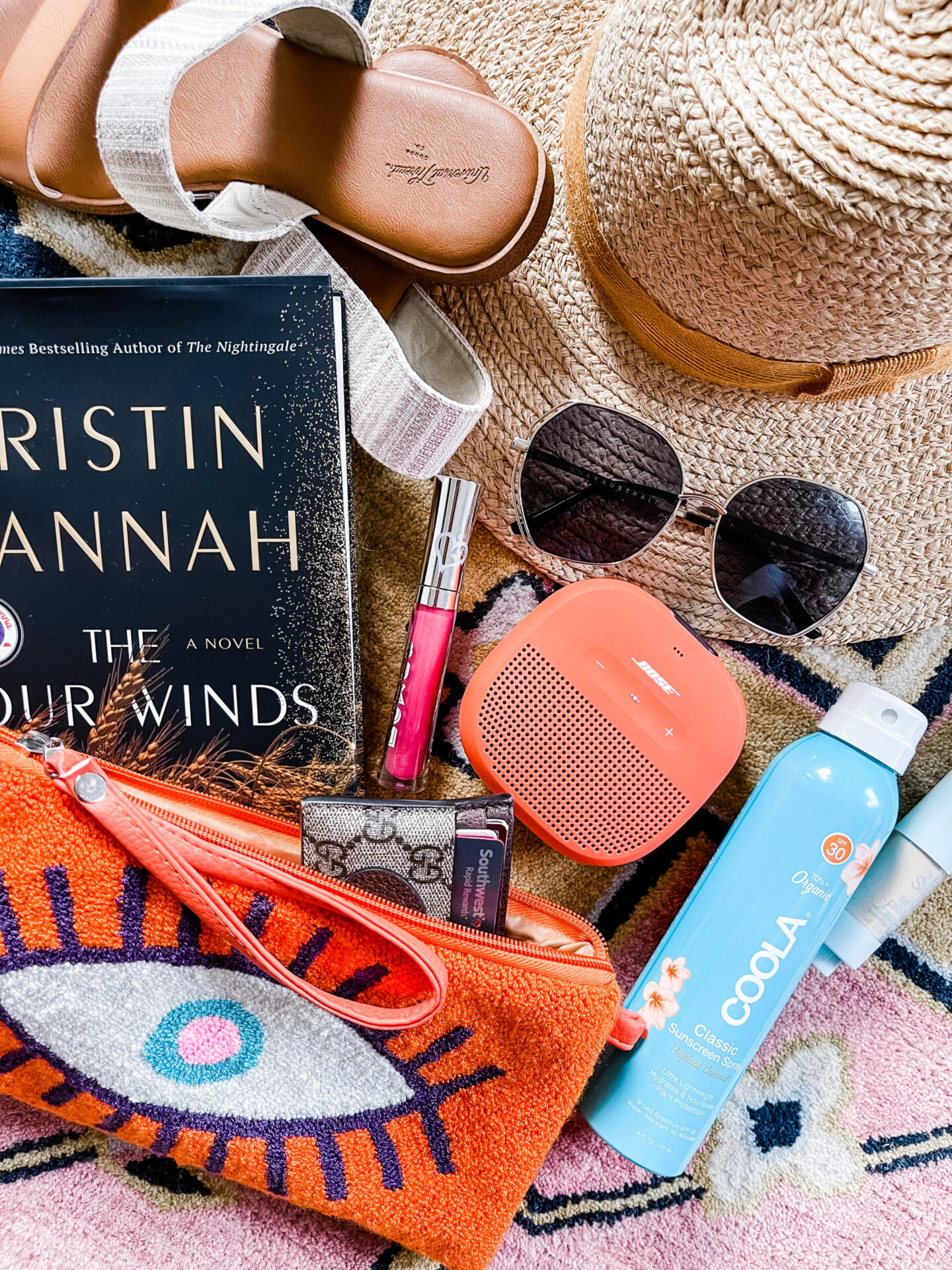 Anthropologie Sale by popular Nashville life and style blog, Hello Happiness: image of an evil eye clutch, straw sunhat, sunglasses, coola spray sunscreen, The Four Winds book, Boxom lipgloss, and a Bose bluetooth speaker.