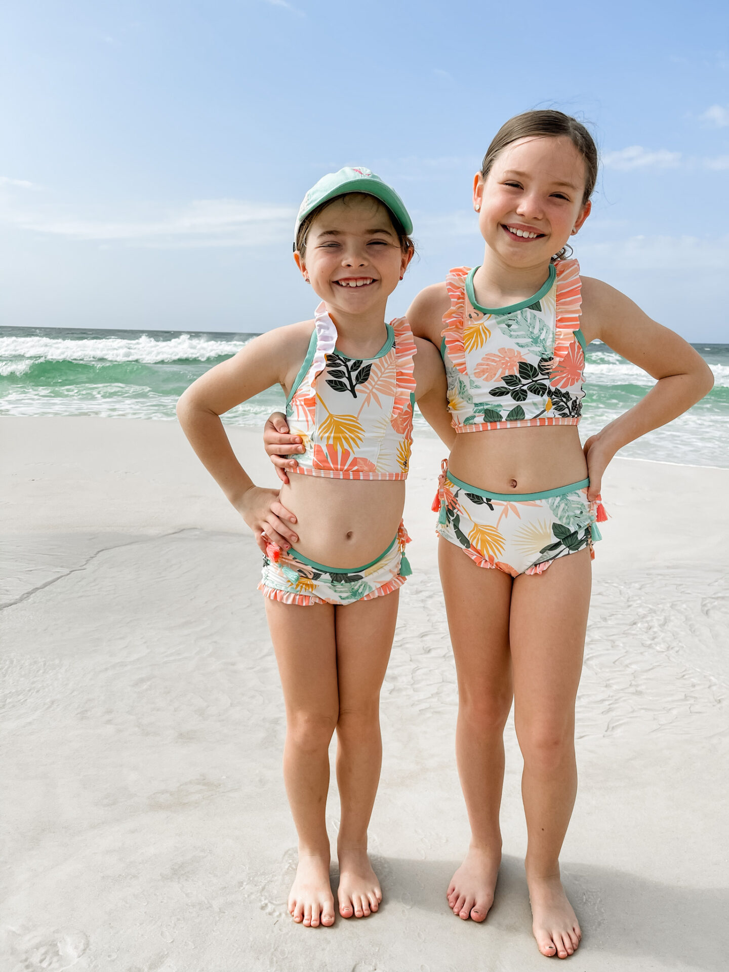 Spring Break Outfits by popular Nashville fashion blog, Hello Happiness: image of two young girls standing together on the beach and wearing On an Island Swimsuits. 
