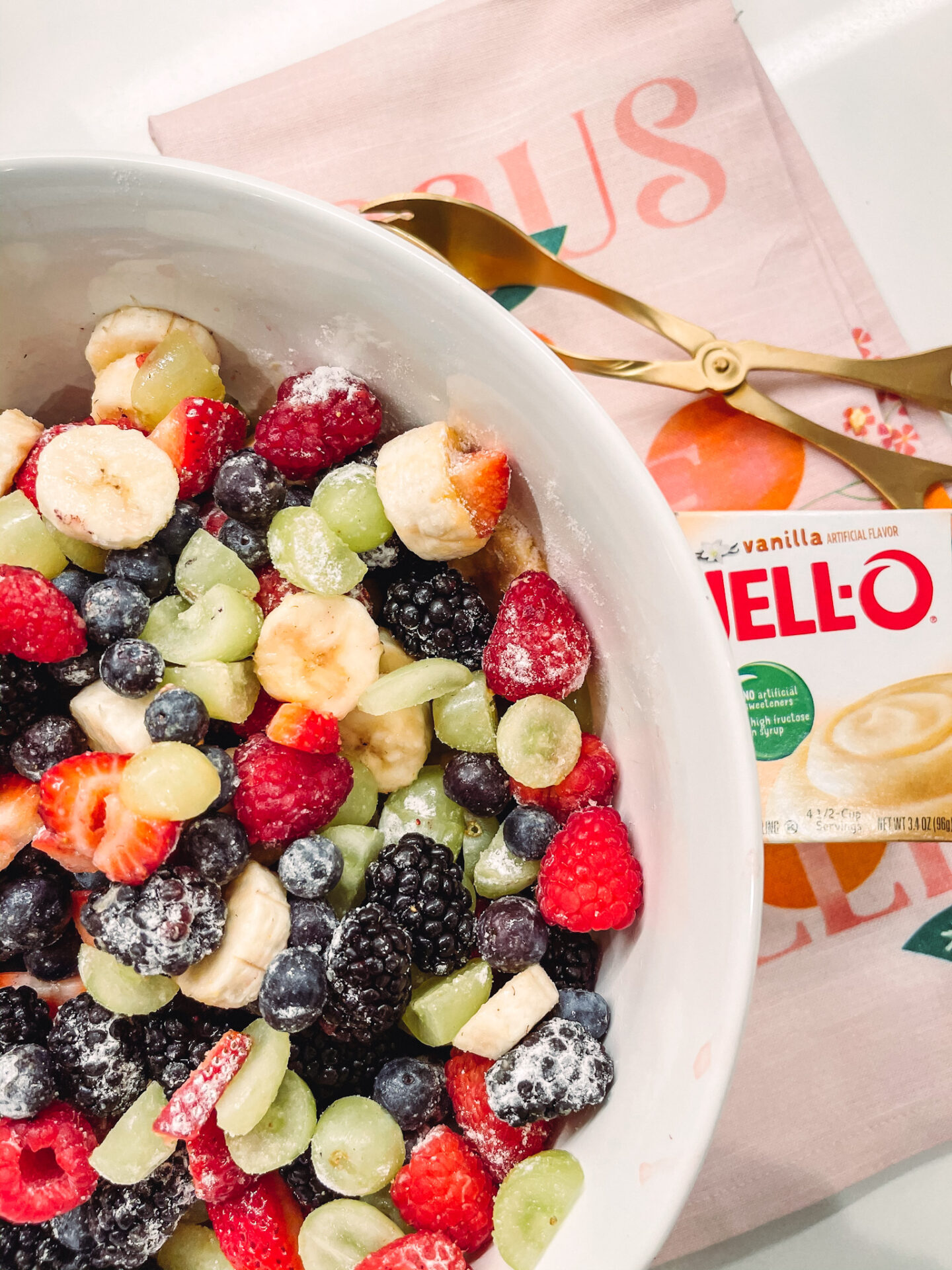 Perfect Fruit Salad by popular Nashville lifestyle blog, Hello Happiness: image of a fruit salad in a white ceramic bowl next to some gold tongs.