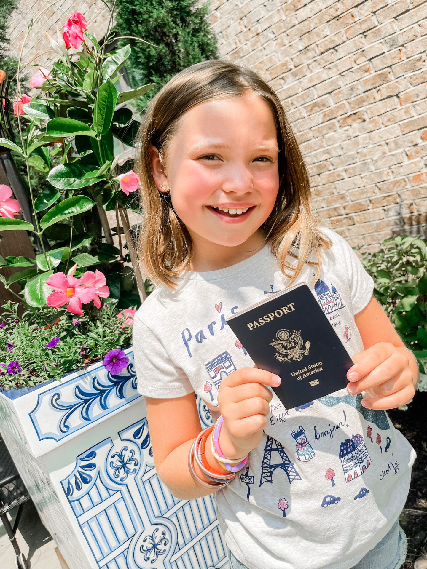 Traveling With Kids by popular Nashville travel blog, Hello Happiness: image of a young girl wearing a Paris graphic t-shirt and holding a passport in her hands.
