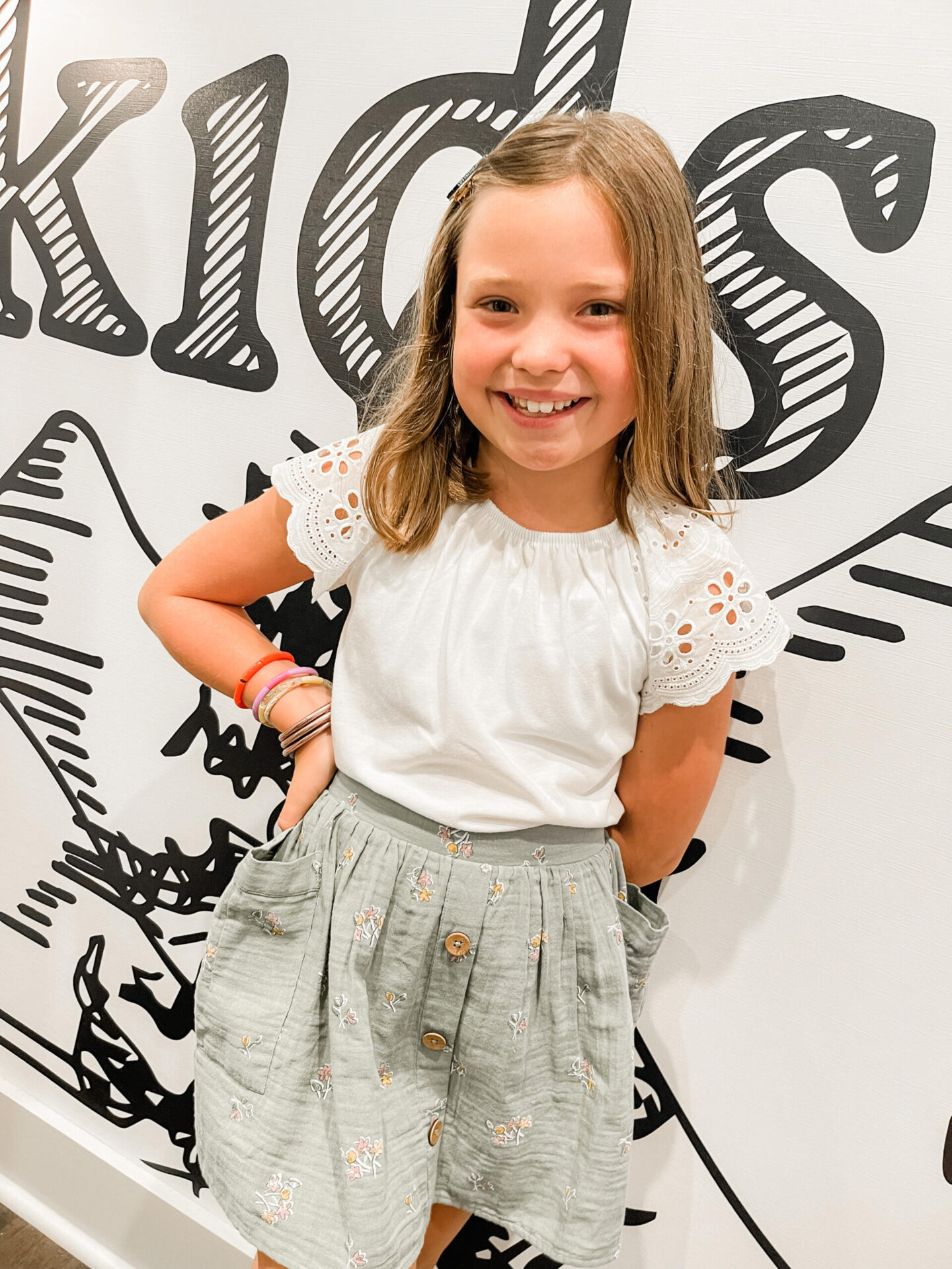 Back to School Essentials by popular Nashville lifestyle blog, Hello Happiness: image of a young girl wearing a white eyelet sleeve top, and grey and pink floral embroidered skirt.