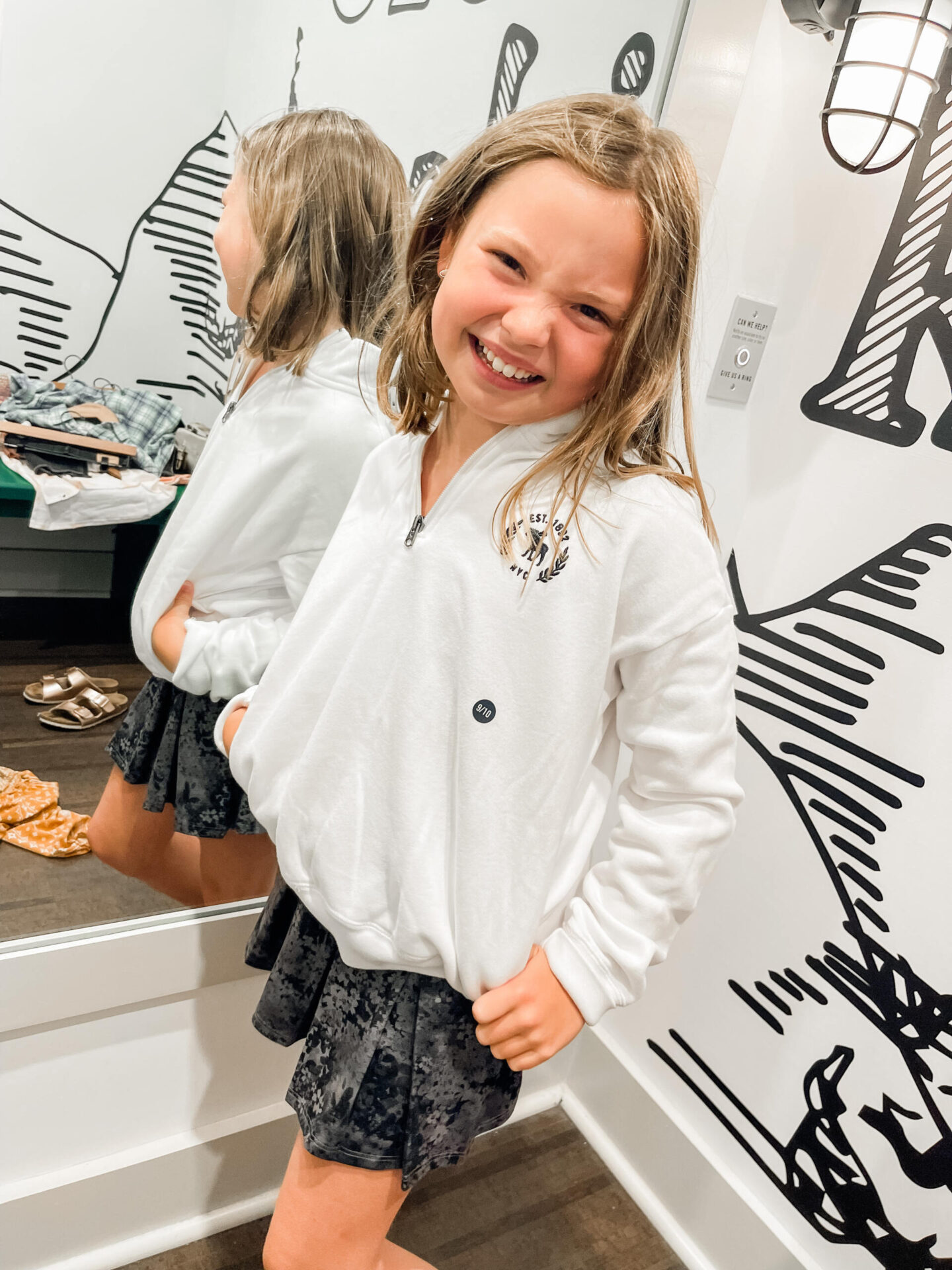 Back to School Essentials by popular Nashville lifestyle blog, Hello Happiness: image of a young girl wearing a white half zip sweatshirt, and black and white floral print pleated skirt.