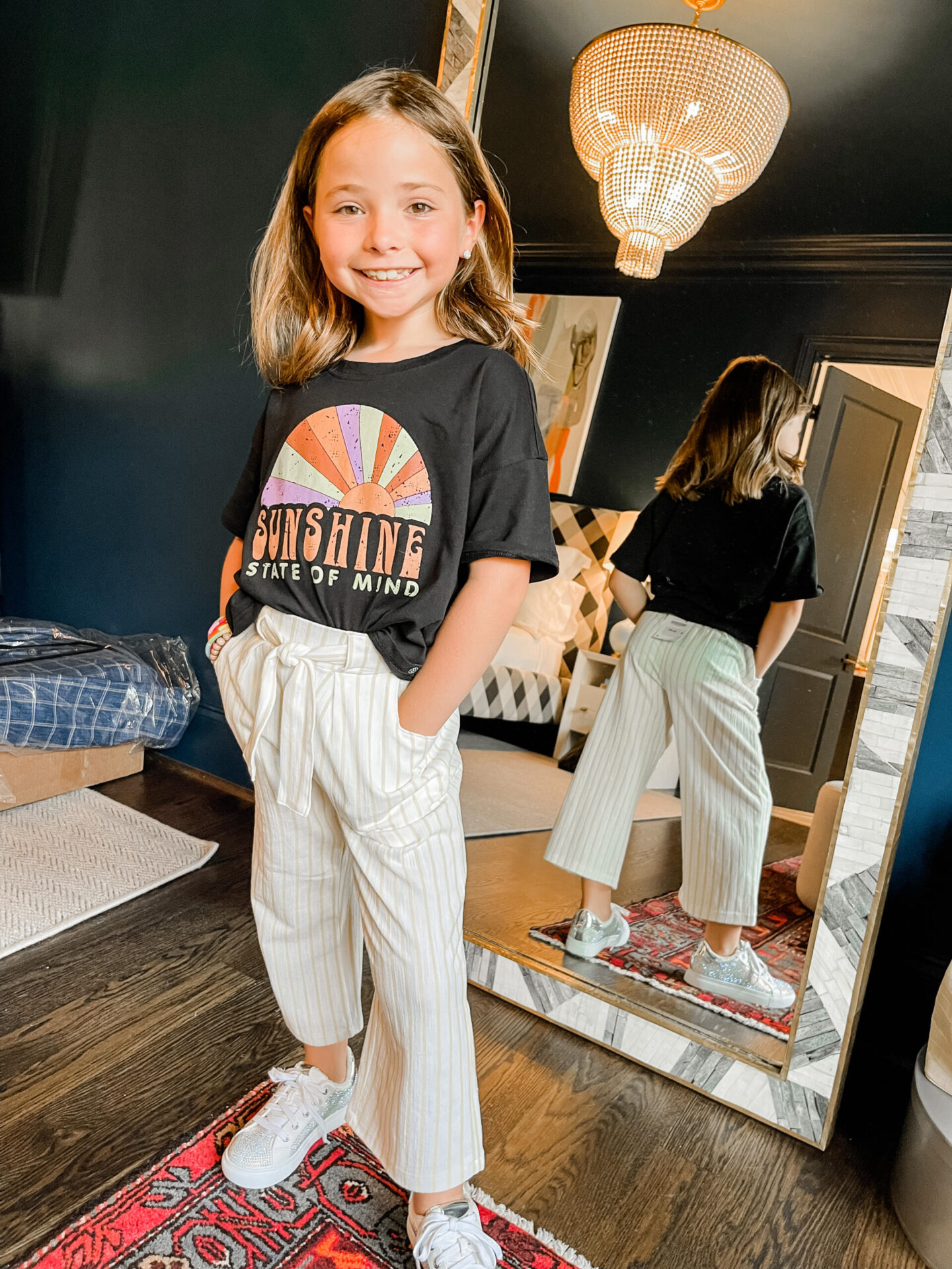 Back to School Essentials by popular Nashville lifestyle blog, Hello Happiness: image of a young girl wearing a Sunshine graphic t-shirt, grey and white tie waste pants and silver glitter sneakers.