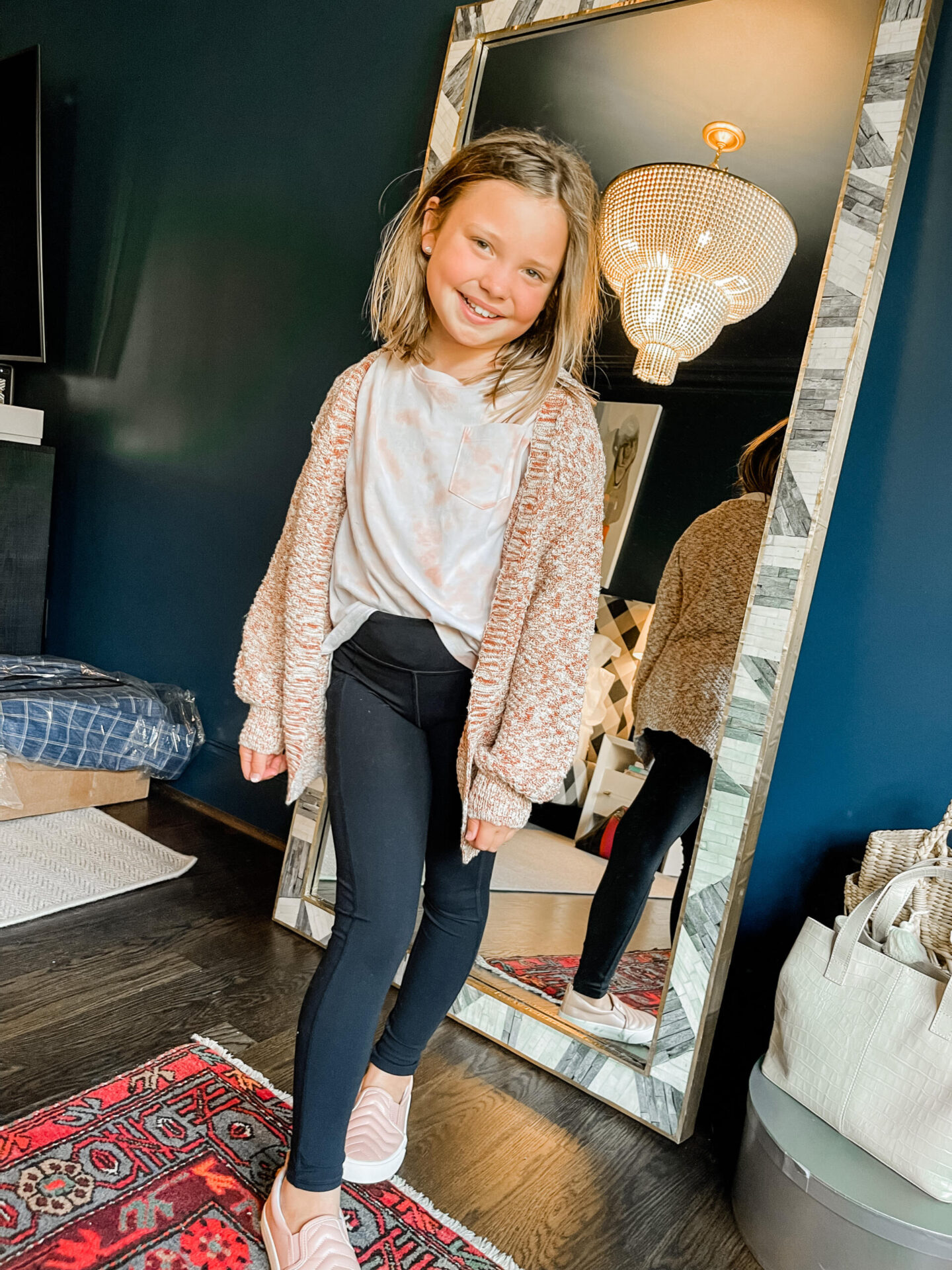 Back to School Essentials by popular Nashville lifestyle blog, Hello Happiness: image of a young girl wearing a peach and white tie dye shirt, black leggings, pink sneakers, and pink and white sweater.