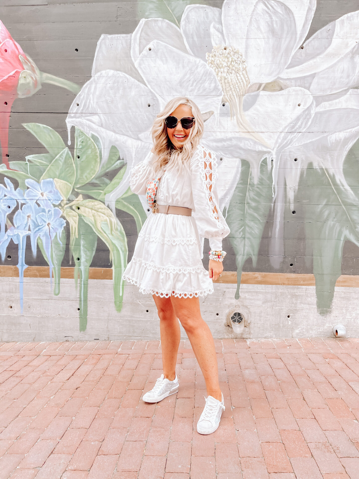 Girls Getaway by popular Nashville travel blog, Hello Happiness: image of Natasha Stoneking standing in front of a floral mural and wearing a white lace trim dress.