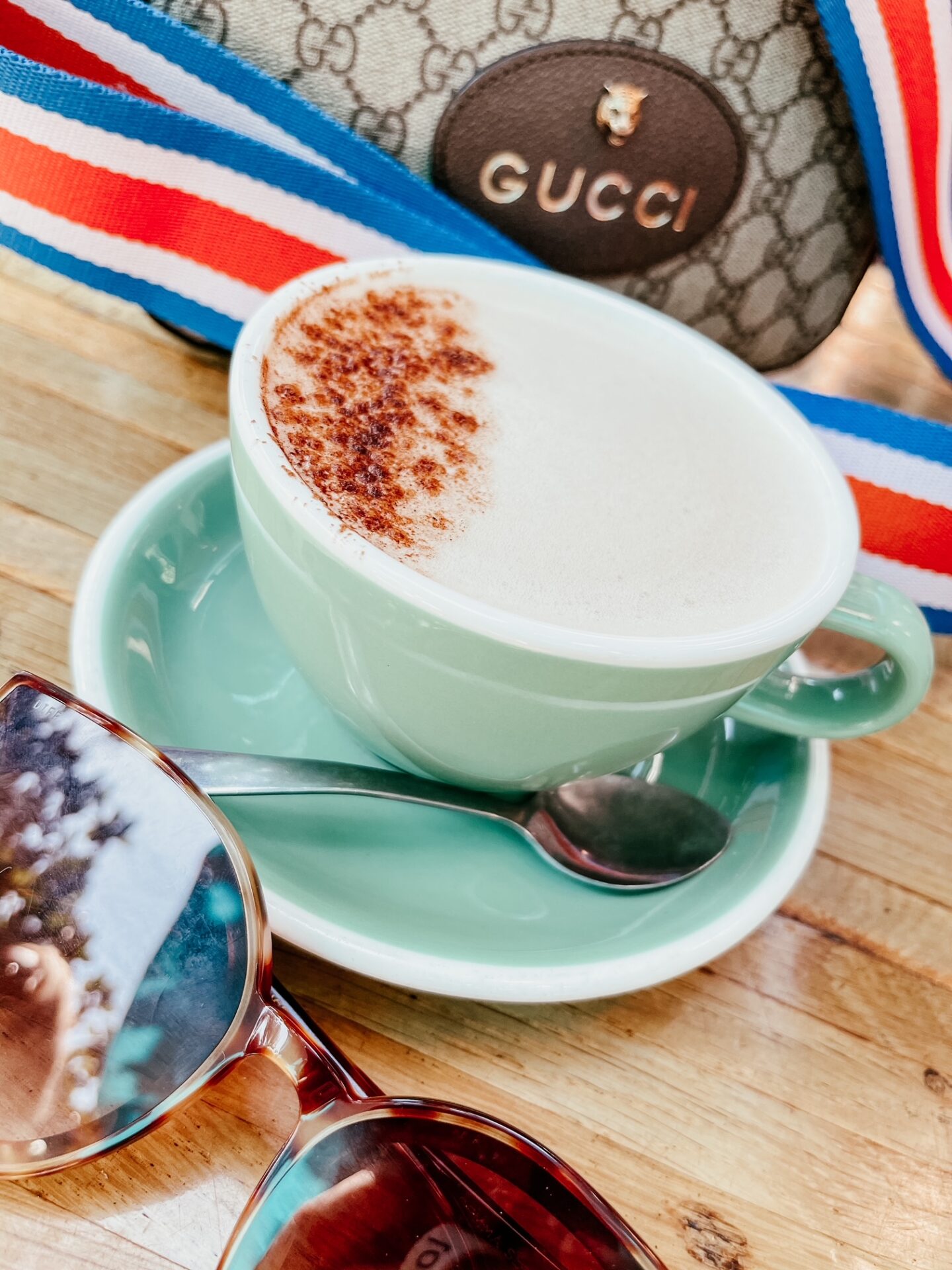 Girls Getaway by popular Nashville travel blog, Hello Happiness: image of a Gucci purse next to a green tea cup and saucer filled with a latte.