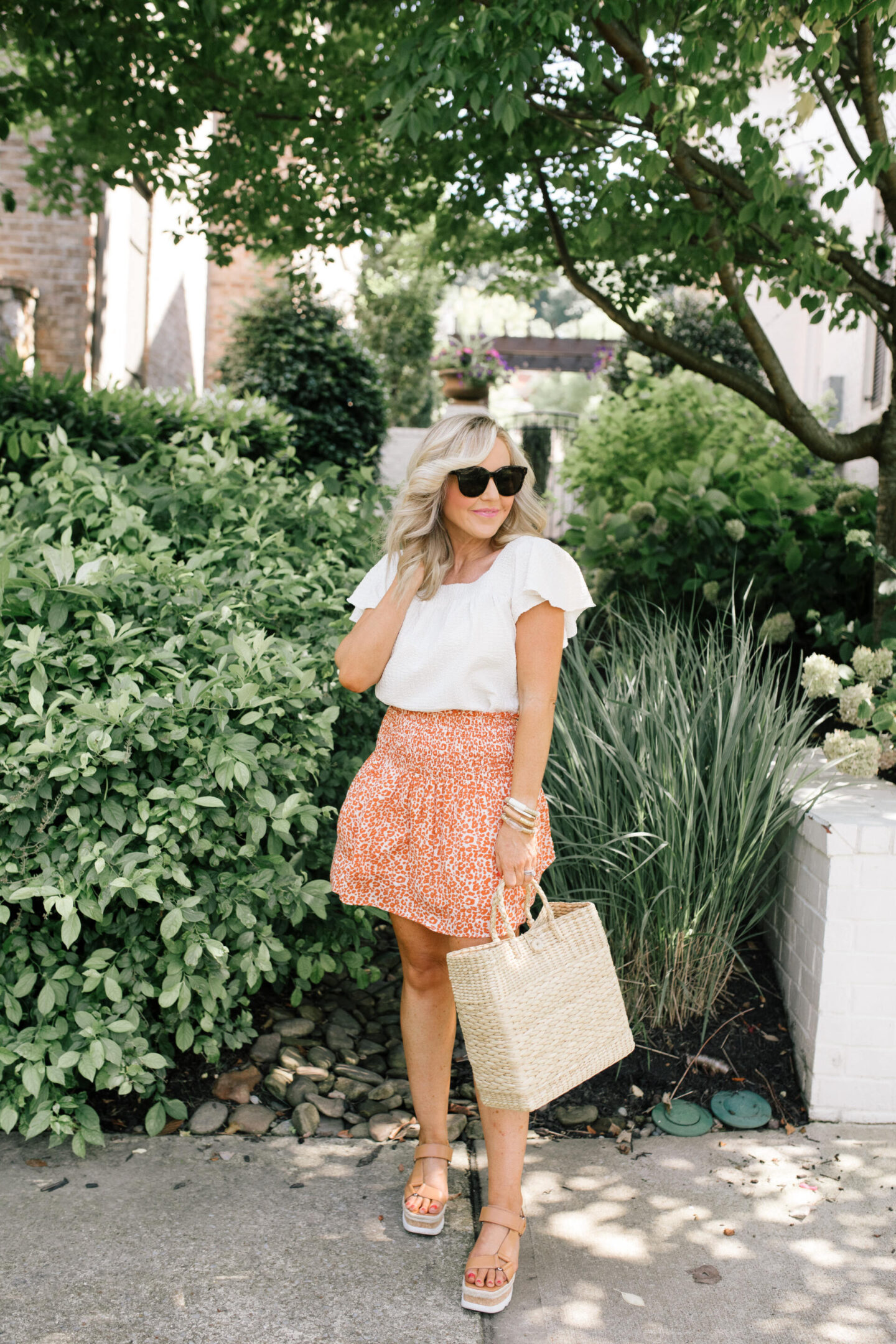 Orange Fashion by popular Nashville fashion blog, Hello Happiness: image of a woman wearing an orange and white floral print skirt and white flutter sleeve top with tan strap platform sandals. 