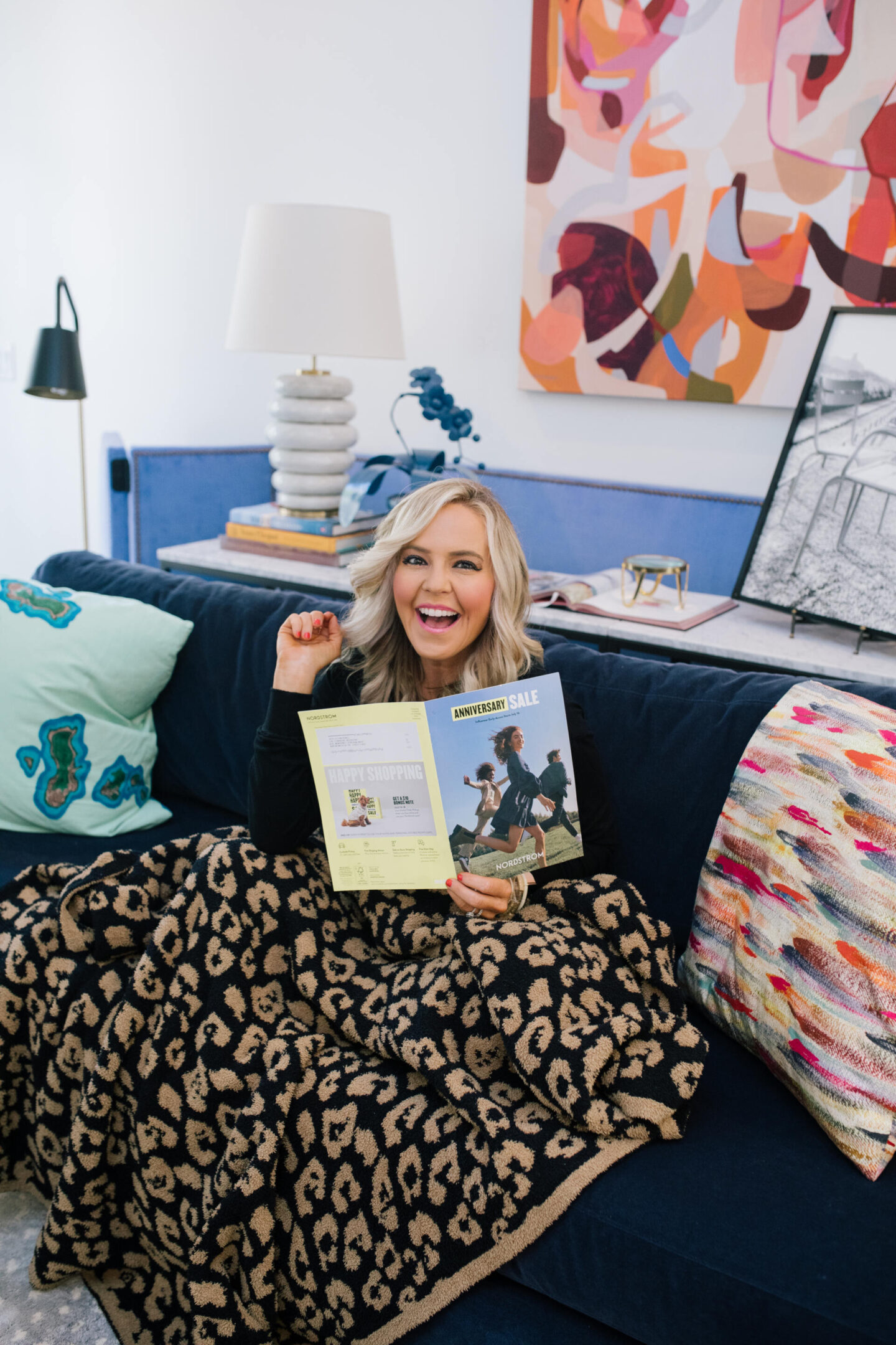 Nordstrom Anniversary Sale by popular Nashville fashion blog, Hello Happiness: image of a woman sitting under a Barefoot Dreams blanket and looking through the Nordstrom Anniversary Sale catalog.