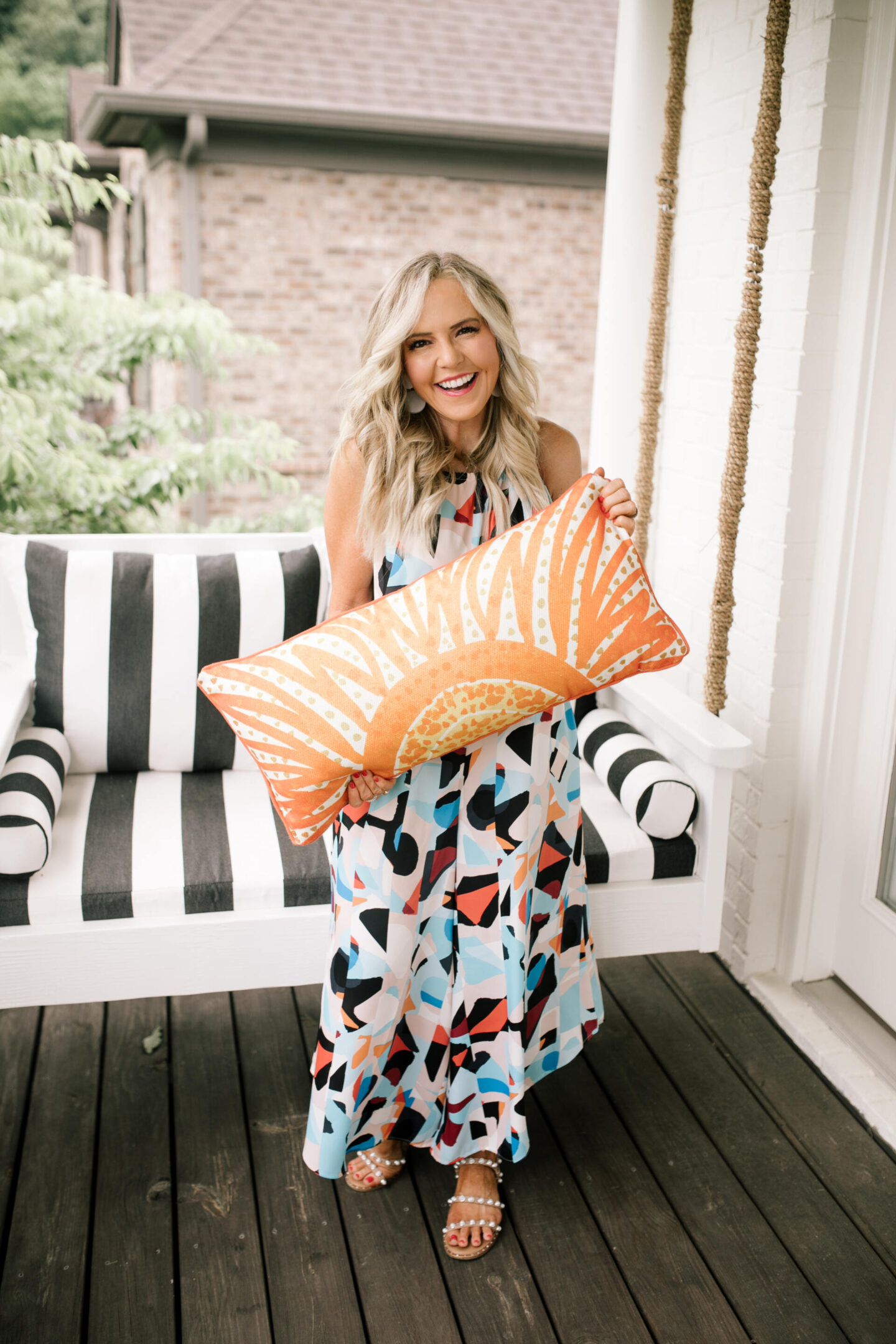 Anthropologie Products by popular Nashville life and style blog, Hello Happiness: image of Natasha Stoneking standing in front of a porch swing with black and white stripe cushions and a orange and cream print lumbar pillow and wearing a geometric prints maxi dress 