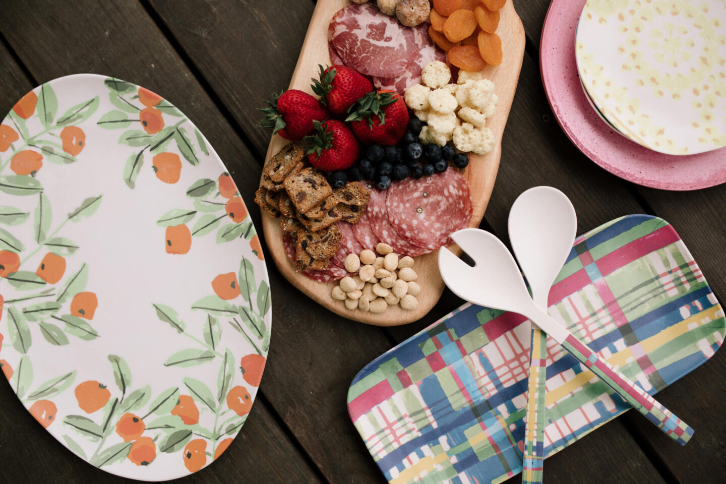 Anthropologie Products by popular Nashville life and style blog, Hello Happiness: image of a wooden serving board filled with sliced meat, strawberries, nuts, blueberries, and dried apricots next to a citrus print oval platter, yellow dot plates, and a plaid rectangular platter and serving utensils with plaid print platters. 