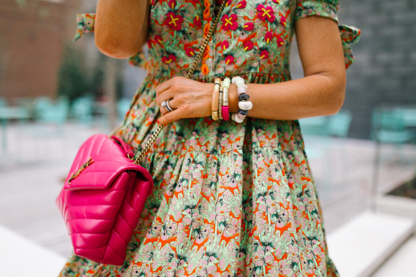 Anthropologie Sale by popular Nashville life and style blog, Hello Happiness: image of Natasha Stoneking standing at a blue outdoor table set and wearing a green floral print dress, camel color strap platform wedge sandals, and a pink YSL bag.