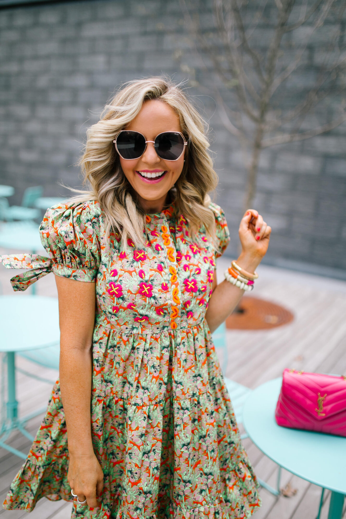 Anthropologie Sale by popular Nashville life and style blog, Hello Happiness: image of Natasha Stoneking standing at a blue outdoor table set and wearing a green floral print dress, camel color strap platform wedge sandals, and a pink YSL bag.