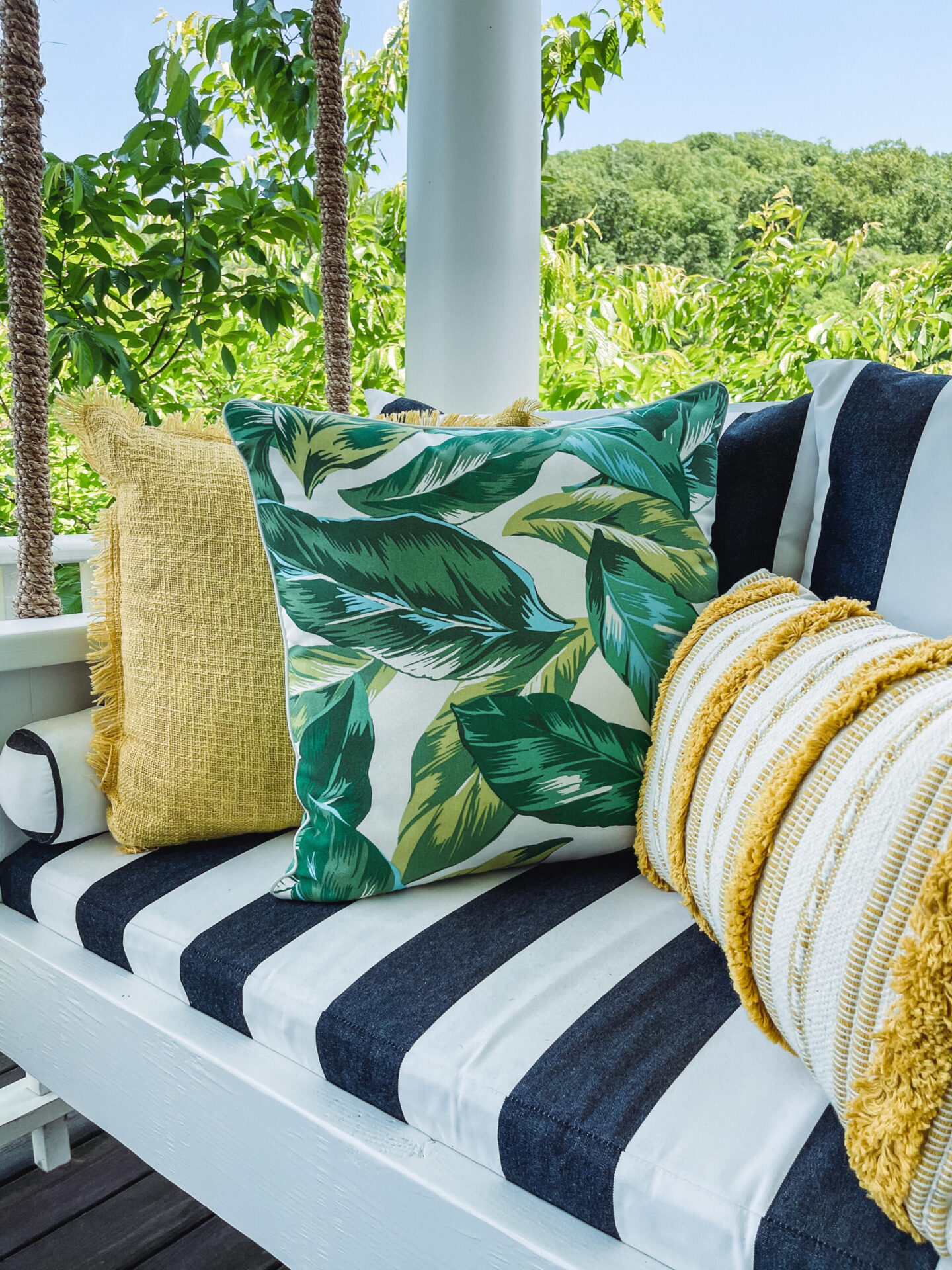 Walmart Summer by popular Nashville life and style blog, Hello Happiness: image of a porch swing with a black and white stripe cushion, yellow fringe throw pillow, palm frond print throw pillow and yellow and white stripe lumbar pillow. 