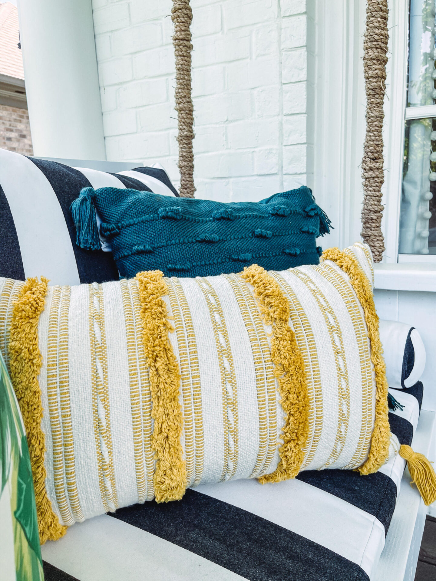 Walmart Summer by popular Nashville life and style blog, Hello Happiness: image of a porch swing with a black and white stripe cushion, yellow fringe throw pillow, palm frond print throw pillow, blue tassel pillow and yellow and white stripe lumbar pillow. 