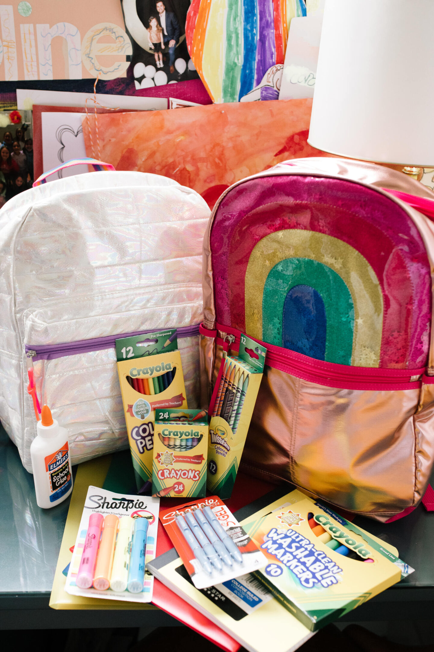 Back to School Essentials by popular Nashville lifestyle blog, Hello Happiness: image of a white iridescent backpack, rainbow backpack, crayon colored pencils, crayola crayons, sharpie highlighters, sharpie pens, craylola markers, Elmer's glue, and notebooks. 