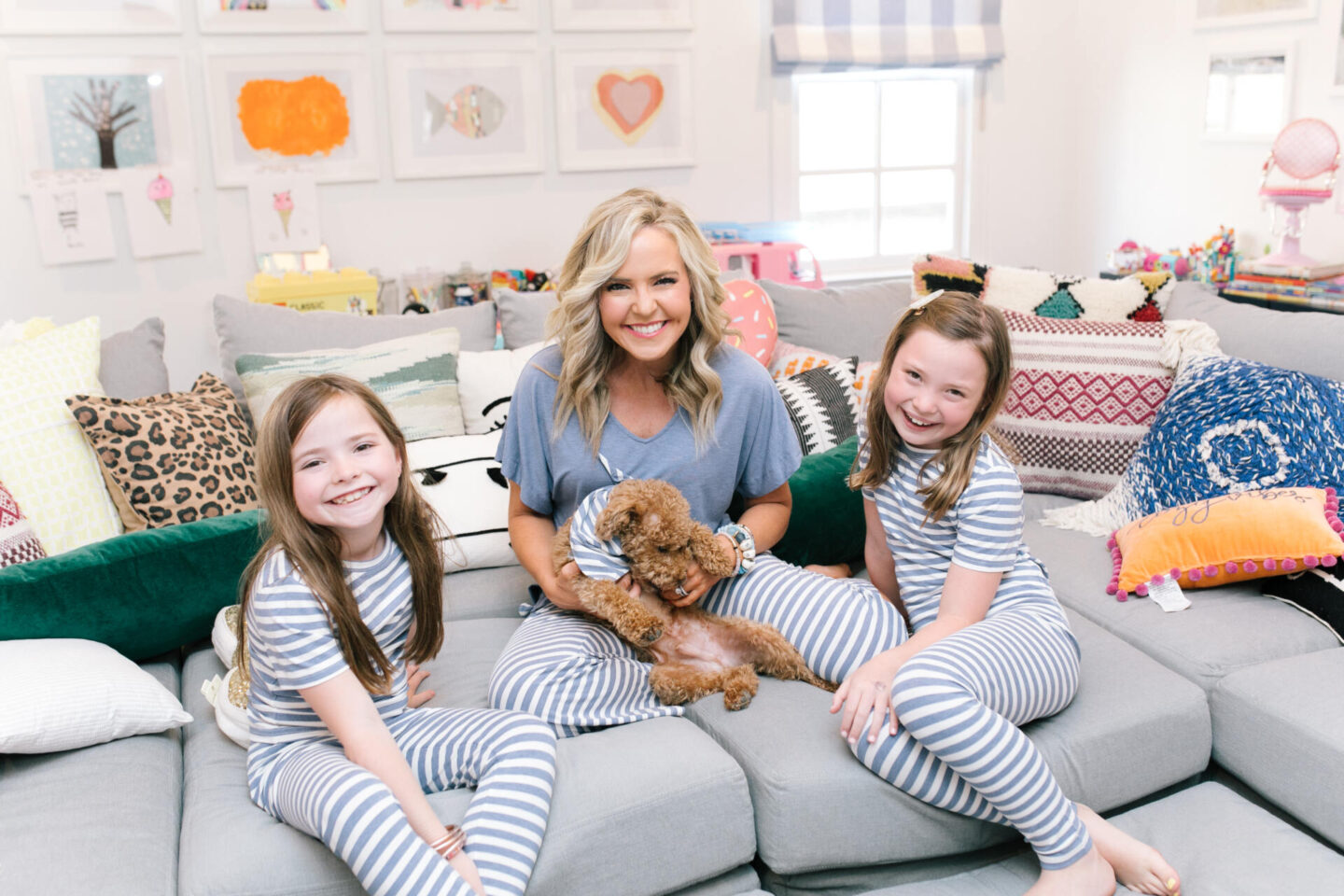 Collaborations and Partnerships by popular Nashville lifestyle blog, Hello Happiness: image of a mom and her tow daughters wearing matching blue and white stripe pajamas and sitting on a grey sectional couch and holding a golden doodle dog. 